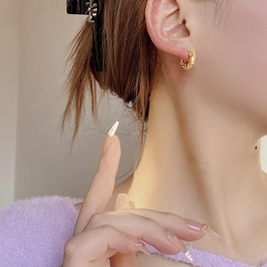 Close-up of golden textured hoop earrings with a hammered finish on model ear
