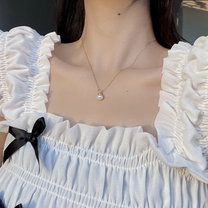 Detailed close-up of a natural pearl pendant on a gold chain worn on the neck