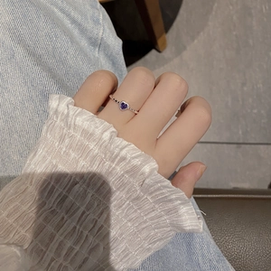 Detail of heart-shaped purple zircon ring with silver twist band on finger