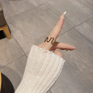 Close-up of minimalist gold wave ring on finger paired with cozy cream knit sweater