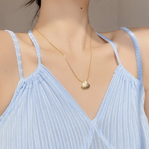 Detail shot of a minimalist gold seashell pendant necklace on a model wearing light blue