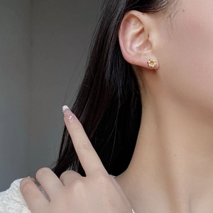 Close-up of polished gold flower stud earring worn by a model showing fine petal details