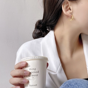 Detail of elegant gold wave earrings worn by a model in a modern urban lifestyle setting