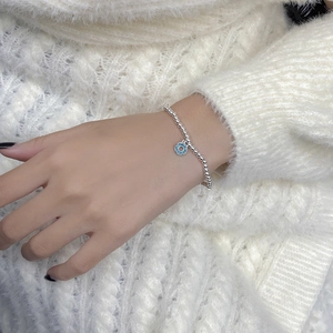 Détail du bracelet en argent massif S925 avec breloque donut bleu sur un pull en maille blanche