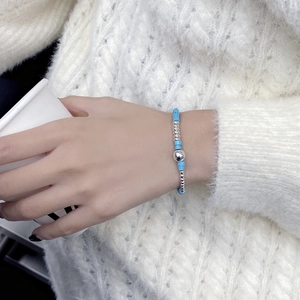 Detailed view of turquoise bead bracelet with silver accents on a cozy white sleeve background