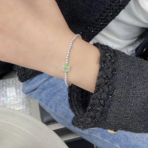 Detail of silver beaded bracelet with green Mahjong charm on wrist with tweed outfit