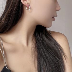 Close-up of a silver twisted knot hoop earring worn by a model with polished finish