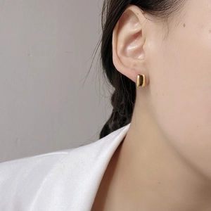 Close-up of elegant gold rectangular hoop earrings worn by a model in a minimalist style