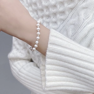Detail of natural baroque pearl bracelet with silver heart clasp on knit sweater sleeve