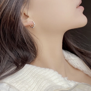 Close-up of geometric S925 sterling silver hoop earrings with twisted metal texture on ear