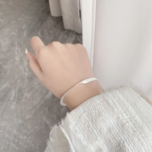 Close-up of minimalist silver open cuff bracelet worn on wrist with elegant white sleeve