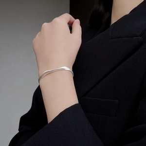 Détail d'un bracelet ouvert en argent mat avec texture ondulée irrégulière sur le poignet
