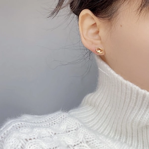 Close-up of gold pig nose stud earrings on model wearing white knitted sweater