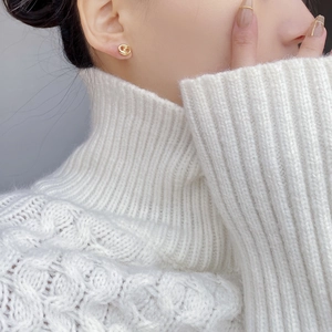 Close-up of a delicate gold pig nose stud earring worn on ear with cozy sweater background