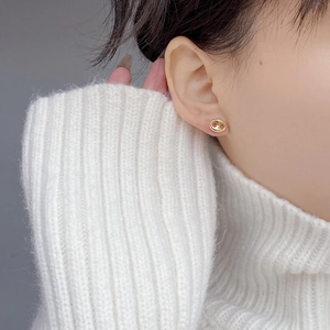Polished gold pig nose earrings worn by model in a cozy white knit sweater