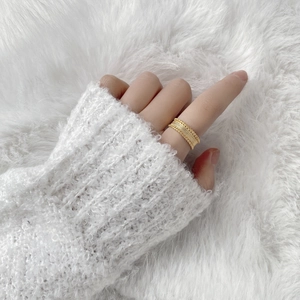Vue détaillée d'une bague dorée large à texture tissée portée sur l'index d'une femme