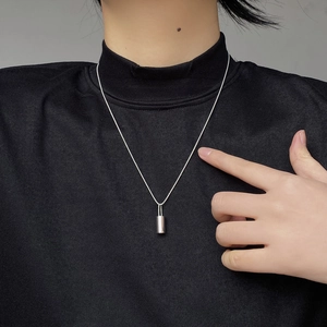 Macro shot of minimalist silver cylinder pendant on ball chain against dark fabric