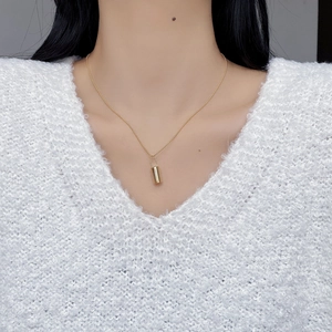 Detail shot of a sleek gold pendant necklace on a soft white knit sweater texture