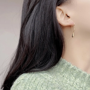 Elegant gold drop earrings with irregular wavy lines and teardrop charm worn by a model