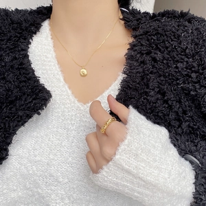 Close-up of golden layered heart necklace and twisted ring on model with white knitwear