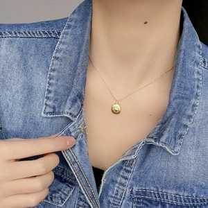 Close-up of golden brushed heart pendant necklace worn on a model with denim jacket