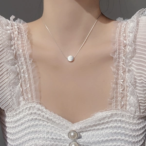 Close-up of brushed silver bean pendant necklace on model with lace blouse