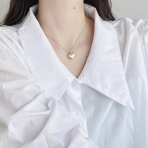 Detail of a gold heart-shaped pendant necklace on a model wearing a white shirt