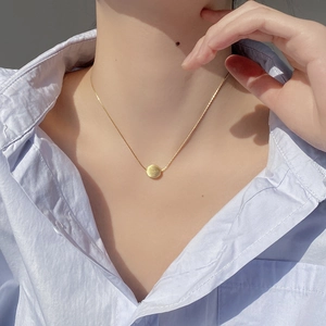 Detail of minimalist brushed gold circle pendant necklace on female model neck