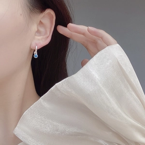 Macro detail of silver turquoise hoop earring worn by model on minimalist background