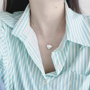 Close-up of heart-shaped mother of pearl pendant on 925 silver chain with striped shirt