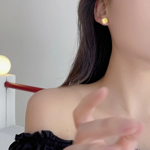 Close-up of a minimalist round gold stud earring shown on a model's ear for size detail
