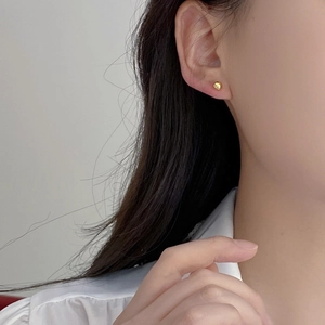 Close-up of a minimalist gold spherical stud earring worn on a female model's earlobe