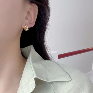 Detailed close-up of a model wearing a gold twisted knot hoop earring in a minimalist style