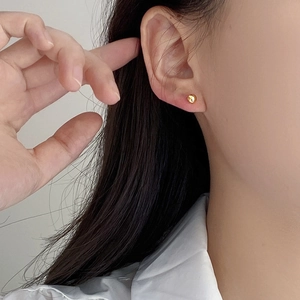 Close-up of minimalist polished gold bead earrings worn on the ear for a subtle look