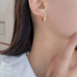 Close-up of a model wearing a gold twisted knot hoop earring with a braided texture design