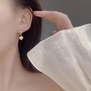 Macro view of golden heart-shaped drop earring worn by a model with elegant detail