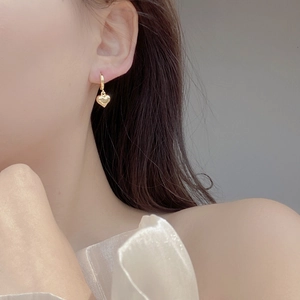 Close-up of model wearing gold heart charm hoop earrings in a minimalist style