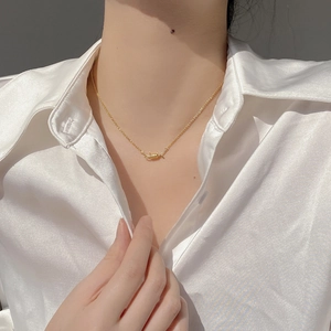 Detailed close-up of a gold thorn wire pendant necklace worn with a white satin shirt