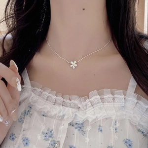 Detail of S925 sterling silver daisy necklace featuring white enamel petals on a model