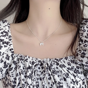 Close-up of a 925 sterling silver bow pendant necklace on a model wearing floral dress