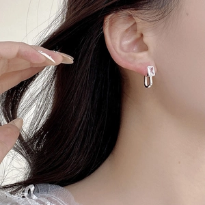 Detail of a geometric silver earring with rectangular zircon on model ear