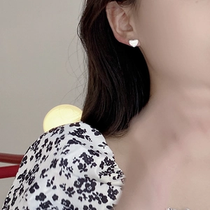 Gros plan de boucles d'oreilles cœur minimalistes en argent S925 portées par une femme