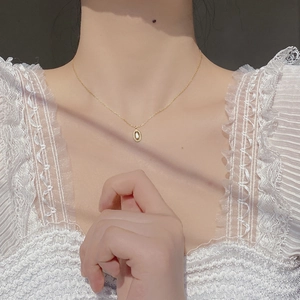Detail of a gold coffee bean pendant on a delicate silver chain worn on the collarbone