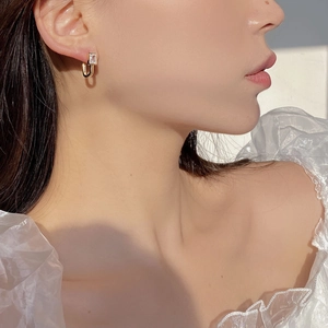 Close-up of a U-shaped gold S925 silver earring with a rectangular zircon on a model