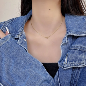Close-up of minimalist gold bead pendant necklace on a delicate chain worn by a model
