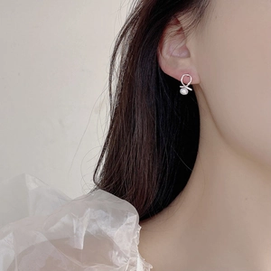Detail of 925 silver cross earring with natural pearl on model in soft lighting