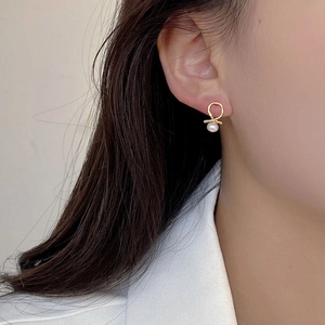 Detail view of gold twist stud earrings with round white pearl on a female model