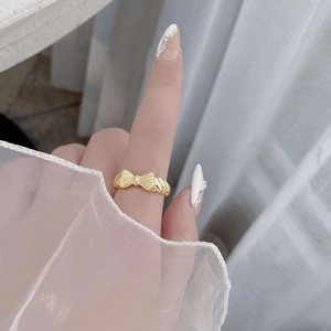 Close-up of golden bow ring with textured finish and twisted band on white backdrop