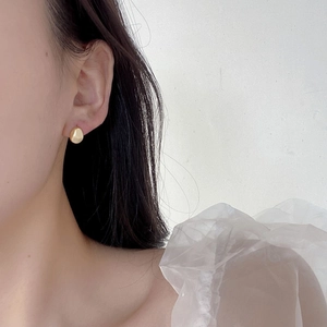 Close-up of minimalist gold pebble earrings worn by a model in elegant white organza