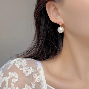 Close-up of elegant S925 silver gold-plated hook earring with a round white pearl on model